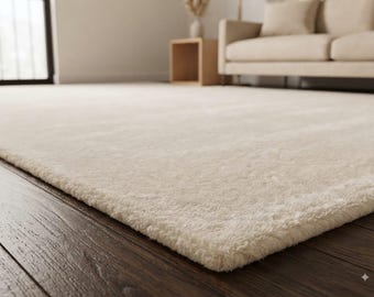 May include: A rectangular area rug with a thick, plush, cream-coloured pile texture. The rug features a soft, dense surface and is positioned flat on a dark brown wooden floor, showcasing its uniform light colour and deep, fuzzy material construction.