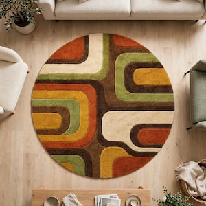 May include: A circular area rug featuring a repeating geometric pattern of interlocking rounded rectangular shapes in shades of burnt orange, mustard yellow, olive green, dark brown, and cream, creating a layered and textured visual effect.