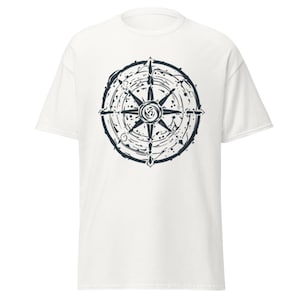 Könnte beinhalten: Ein weißes Kurzarm-T-Shirt mit einer mittigen, schwarzen Grafik einer stilisierten Kompassrose. Das Design besteht aus kreisförmigen Ringen und strahlenden Spitzen mit einer verwaschenen, tintenspritzerartigen Textur auf dem Stoff.