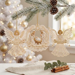 Può includere: Tre decorazioni natalizie in pizzo color crema appese a un ramo di pino. Due sono angeli con capelli dorati e striscioni con la scritta "PEACE ON EARTH" e "HOPE & LOVE & PEACE". L'ornamento centrale raffigura un presepe con "Merry Christmas 2026".