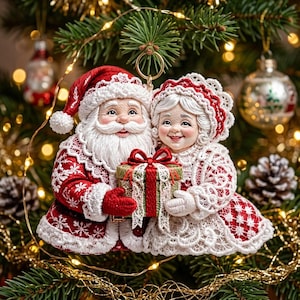 Può includere: Un addobbo per albero di Natale raffigurante Babbo Natale e la Signora Natale che tengono in mano un piccolo regalo. Babbo Natale indossa un cappotto rosso con bordi in pizzo bianco e un cappello abbinato. La Signora Natale indossa un abito in pizzo.