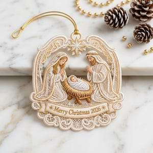 Puede incluir: Un adorno navideño de encaje color crema que presenta una escena de natividad con figuras de María, José y el niño Jesús en un pesebre. El diseño incluye una estrella en la parte superior y una cinta en la base con el texto Merry Christmas 2026.
