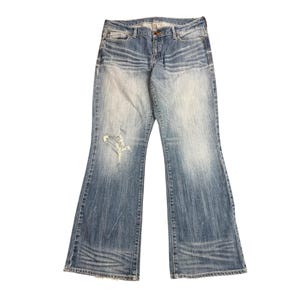 Op de afbeelding: Lichtblauwe spijkerbroek van denim met een bootcut-model, een taille met gemiddelde hoogte en een verwassen afwerking met whisker-patronen op de heupen en bovenbenen. De voorkant van de linkerpijp heeft een enkele gerafelde scheur boven de knie.