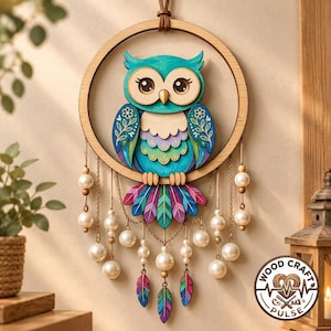 Op de afbeelding: Een ronde houten wandhanger met een gelaagde uilenillustratie in tinten blauwgroen, paars en groen. De uil is gecentreerd in een houten ring, geaccentueerd met bungelende gouden kettinkjes, witte parelachtige kralen en kleurrijke veerbedels.
