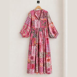 May include: A long-sleeved midi dress featuring a vibrant patchwork design in various shades of pink. The garment displays a mix of floral, geometric, and checkered patterns throughout, with a button-down front and a relaxed, flowing silhouette.