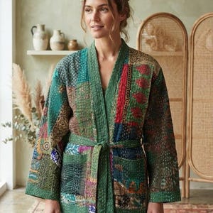 Puede incluir: Una chaqueta acolchada con diseño de patchwork que combina diversos patrones de tela en tonos verdes, rojos y azules. La prenda cuenta con mangas largas, un cinturón para anudar a la cintura y dos bolsillos frontales con costuras visibles.