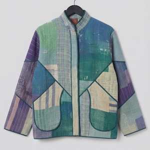 Könnte beinhalten: Eine langärmelige Jacke mit Patchwork-Design in Blau-, Grün- und Violetttönen. Das Kleidungsstück verfügt über einen Stehkragen, eine Knopfleiste auf der Vorderseite und zwei große aufgesetzte Taschen mit dunkler Einfassung.