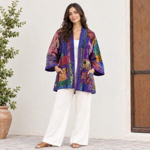 Könnte beinhalten: Eine langärmelige Jacke mit offener Vorderseite und Patchwork-Design, bestehend aus verschiedenen bunten Mustern in Violett, Blau, Gelb und Rot. Die Jacke hat zwei Vordertaschen und wird über einem weißen Oberteil und einer weißen Hose getragen.