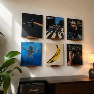 May include: Six vinyl record album covers displayed on a wall using small wooden wall mounts. The collection includes The Dark Side of the Moon, Abbey Road, What's Going On, Nevermind, The Velvet Underground & Nico, and The Doors self-titled album.