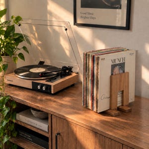May include: A light wood record player with a clear plastic dust cover and a black turntable platter, positioned next to a wooden record stand holding a collection of vinyl records with a white cover featuring the text MUNCH.