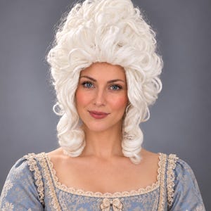 以下が含まれることがあります： ボリュームのあるタイトなカールヘアが特徴の白いウィッグ。高く丸みを帯びた形状で、サイドには段状のリングレットが流れています。花柄の青いドレス、スクエアネック、ベージュのレーストリムと組み合わされています。