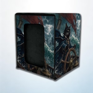 Op de afbeelding: Een vierkante opbergdoos met een grafische illustratie van een zwarte kat verkleed als kapitein, die een schip bestuurt door een stormachtige oceaan met hoge golven, donkere wolken en rode zeilen onder een onweerslucht.