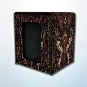 May include: A rectangular deck box featuring a dark, intricate illustration of pale, elongated hands reaching toward a glowing orb beneath a floating pyramid with an eye. The design includes thorny vines and deep red and black tones.