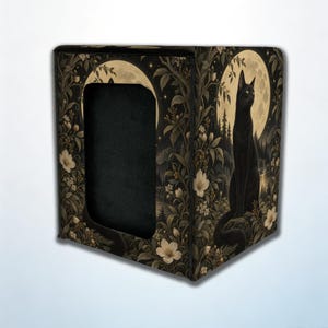 May include: A square storage box featuring a black cat sitting in a forest landscape under a large full moon. The design includes detailed foliage, white flowers, and a dark, solid black rectangular cutout on the front panel.