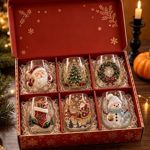 May include: A set of six clear stemless glasses housed in a red gift box with gold snowflake patterns. Each glass features a distinct raised holiday design: a Santa Claus, a Christmas tree, a wreath, a stocking, a sleigh, and a snowman.