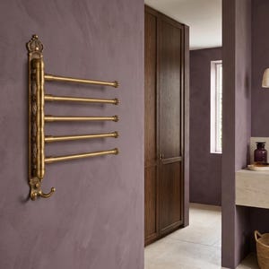 Puede incluir: Un toallero de pared de latón con cinco brazos horizontales giratorios y un detalle decorativo en forma de corona en la parte superior. El accesorio incluye un gancho curvo en la parte inferior, con un acabado metálico cepillado.