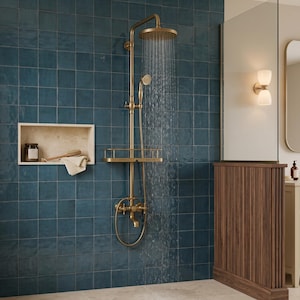 May include: A brass shower system with a round overhead rainfall showerhead and a handheld sprayer, mounted on a dark blue tiled wall. The system includes a built-in shelf and is actively dispensing water. A recessed niche holds a bottle and cloth.