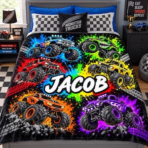 May include: A black plush blanket featuring a vibrant, multi-colored monster truck theme with splashes of neon paint. The design includes five distinct monster trucks in blue, green, red, yellow, and purple, with the name JACOB in white text.