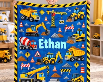 May include: A blue fleece blanket featuring a construction theme with yellow dump trucks, excavators, cranes, and cement mixers. The design includes orange traffic cones, warning signs, and piles of dirt. The name Ethan is printed in large light blue letters.