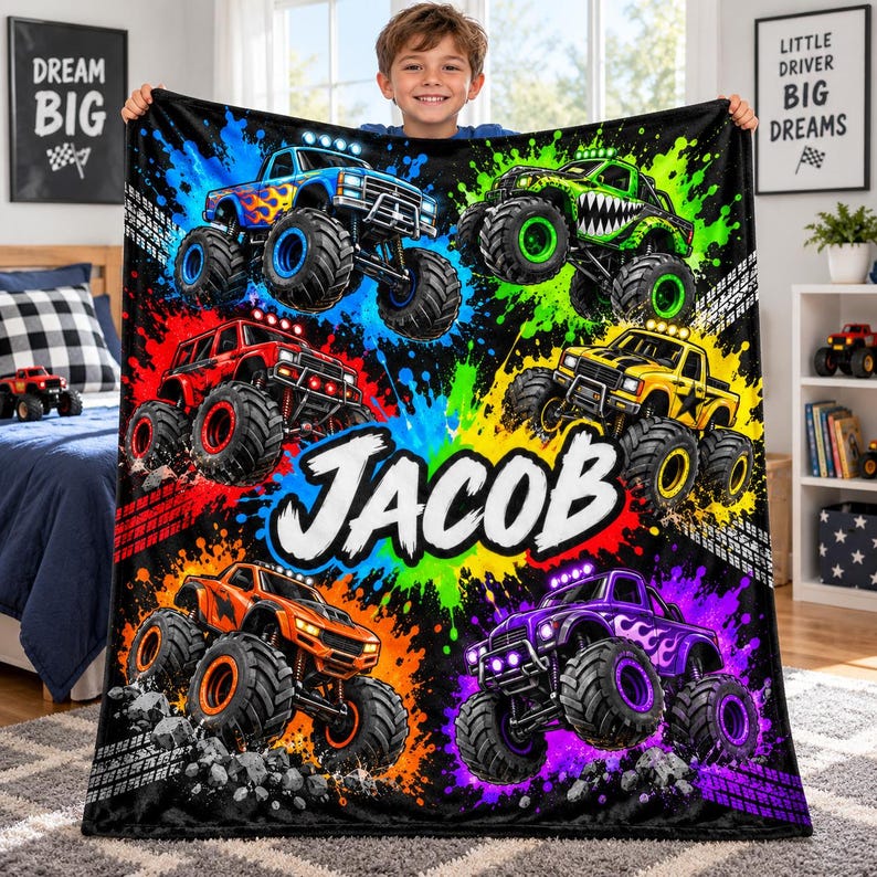 May include: A soft plush blanket featuring a vibrant, multi-colored paint splatter background with five monster trucks in blue, green, red, yellow, and purple. The name JACOB is printed in large, bold white letters across the center of the blanket.