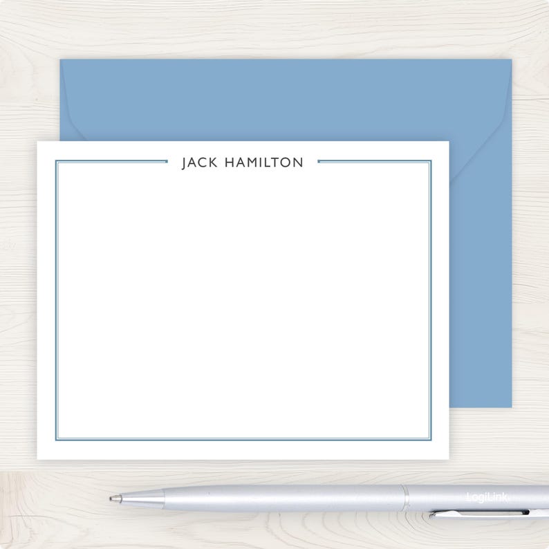 A blank white card with the name "JACK HAMILTON" written on it, placed on top of a blue envelope, with a pen lying next to the card.