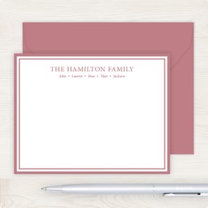 May include: Stationery set featuring a mauve-colored envelope and a matching note card. The card has a white interior with a mauve border and the text "THE HAMILTON FAMILY" with names below. A silver pen rests below.