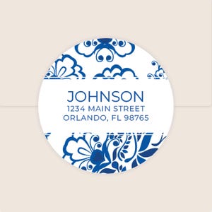 May include: A round white sticker with a blue floral design border. The text "JOHNSON" is in a bold blue font, with address details below. The sticker is on a light beige background.