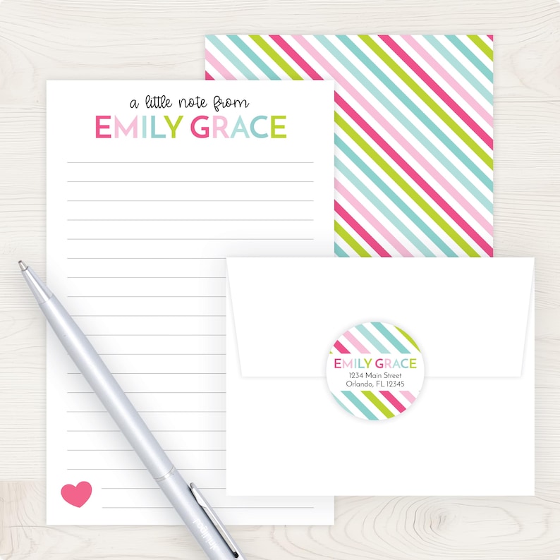 a white envelope with a heart-shaped label, a blank lined paper, and a pen on a wooden surface.