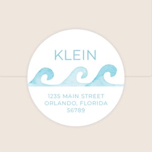 May include: A round sticker with a light blue watercolor wave design. The name "KLEIN" is printed in light blue above the waves. Below the waves, the address "1235 MAIN STREET ORLANDO, FLORIDA 56789" is printed in light blue.