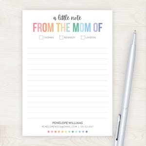 May include: A white notepad with the text "a little note FROM THE MOM OF" in colorful letters. Below are checkboxes for "THOMAS", "KENNEDY", and "LANDON". The notepad has lined pages and a silver pen rests on the right side.