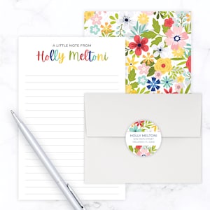 May include: A white lined notepad with the text "A Little Note From Holly Meltoni" at the top. A white envelope with a floral round sticker that says "Holly Meltoni, 1234 Main Street, Orlando, FL 12345".