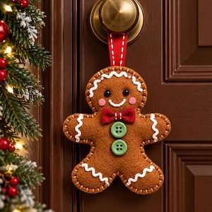 May include: A brown felt gingerbread man ornament hanging from a brass doorknob by a red ribbon. The figure features white stitched icing details, two green buttons on the torso, a red felt bow tie, pink cheeks, and black bead eyes.