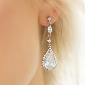 May include: Silver teardrop earrings with a large pear-shaped crystal surrounded by smaller crystals.