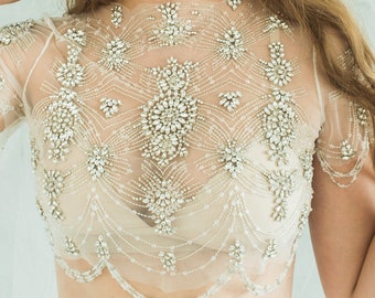 May include: A sheer, beaded top with a high neckline and short sleeves. The top is adorned with intricate patterns of rhinestones and sequins.