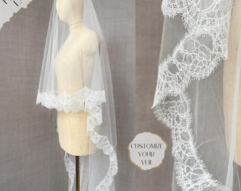 May include: A white bridal veil with a delicate lace trim. The veil is made of soft tulle and has a scalloped edge. The lace trim is intricate and features a floral design. The veil is shown on a mannequin, with the text "CUSTOMIZE YOUR VEIL" visible in the background.
