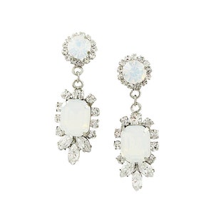 May include: A pair of elegant drop earrings with a silver-tone metal setting. Each earring features a large, rectangular, opalescent stone surrounded by smaller clear crystals. A smaller, round opalescent stone is at the top, also encircled by crystals.