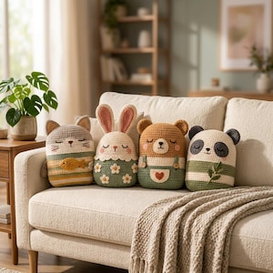Pode incluir: Quatro almofadas de pelúcia em crochê com formas de animais, incluindo um gato com um peixe, um coelho com flores, um urso com jardineiras e um panda com uma folha. Cada almofada apresenta uma paleta de cores única em fio creme, verde, castanho e bege.