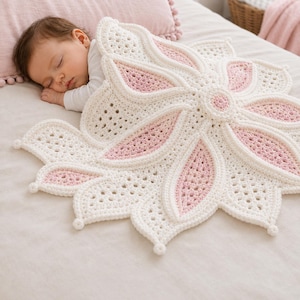 Può includere: Una coperta circolare all'uncinetto con un grande motivo floreale a più petali in filato color crema e rosa tenue. La coperta presenta un motivo a punti traforati e testurizzati con piccoli dettagli a pallina sulle punte di ogni petalo.