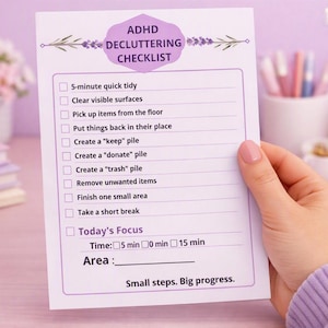 Può includere: Una lista di controllo per il decluttering ADHD su carta bianca con testo viola e accenti floreali. Include attività come 5-minute quick tidy, clear visible surfaces e create a keep pile, terminando con Small steps. Big progress.