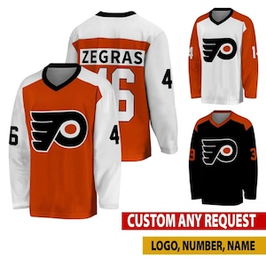 Peut inclure: Trois maillots de hockey arborant le logo des Philadelphia Flyers. Un maillot est orange avec des manches blanches, un est blanc avec des manches orange, et un est noir avec des épaules orange. Les maillots portent le nom Zegras et le numéro 46.