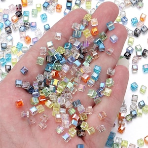 Puede incluir: Una gran colección de pequeñas cuentas de vidrio en forma de cubo con un acabado iridiscente. Las cuentas presentan una variedad de tonos translúcidos que incluyen azul, verde, amarillo, naranja y tonos claros, cada una con un orificio central.