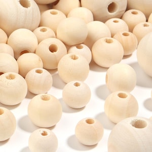 May include: A collection of numerous round, light-colored wooden beads of varying sizes. Each bead features a smooth, unfinished surface and a central hole drilled through the middle, showcasing the natural grain and texture of the light wood.