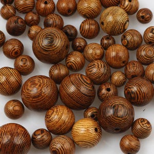 May include: A collection of spherical wooden beads in various sizes, each featuring a distinct dark brown and tan wood grain pattern with visible circular rings and a small drilled hole through the centre of each individual bead.
