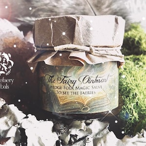 May include: A small glass jar labeled "The Fairy Ointment" with a paper lid. The jar's label features an open book illustration and the text "Hedge Folk Magic Salve To See The Faeries." The jar is surrounded by moss and crystals.