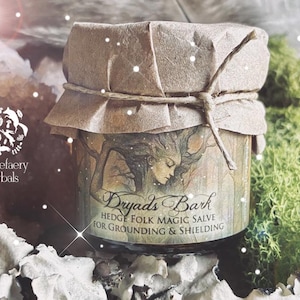 May include: A small glass jar of "Dryads Bark" hedge folk magic salve, wrapped in brown paper and tied with twine. The label features an illustration of a woman and the text "for grounding & shielding". The jar is surrounded by moss and crystals.