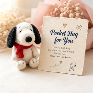 May include: A small white plush dog with black ears and a red scarf next to a rectangular card with deckled edges. The card features the text "Pocket Hug for You" along with a sun icon, two small hearts, and a small illustration of the same dog.