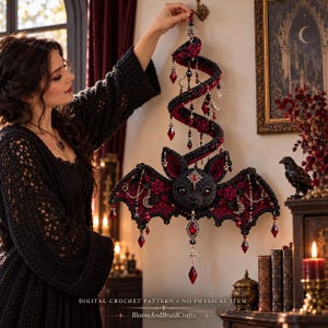 May include: A black and dark red crocheted bat wall hanging featuring a spiral tail, adorned with red roses, silver crescent moon charms, star accents, and faceted red crystal beads. Text at the bottom reads: DIGITAL CROCHET PATTERN • NO PHYSICAL ITEM