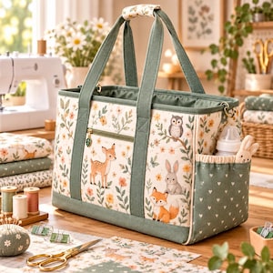 Può includere: Una borsa tote rettangolare in tessuto con sfondo color crema e un motivo di cervi, conigli, volpi, gufi e fiori. La borsa presenta finiture verde salvia, due manici robusti, una tasca frontale con cerniera e un ciondolo a forma di foglia.