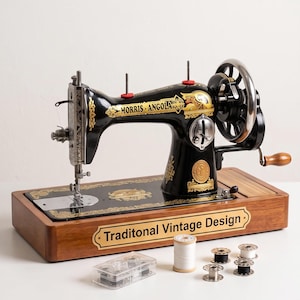 Può includere: Una macchina da cucire nera con motivi decorativi dorati e la scritta MORRIS ANGOLA, montata su una base in legno con una targhetta recante la scritta Traditonal Vintage Design. Include una scatola di plastica con bobine e rocchetti.