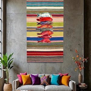 May include: A rectangular wall tapestry featuring a series of horizontal stripes in various colours including red, blue, green, yellow, and cream. A vertical stack of seven fish in shades of red, blue, and silver is centred on the tapestry.